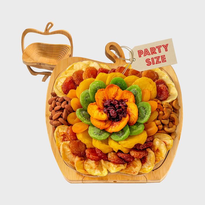 Fruit and nuts are artistically arranged on a wooden apple-shaped tray, with a 