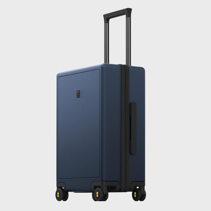 Suitcase stands upright; handle extended. It features four wheels and a blue exterior. Background is plain and light gray.