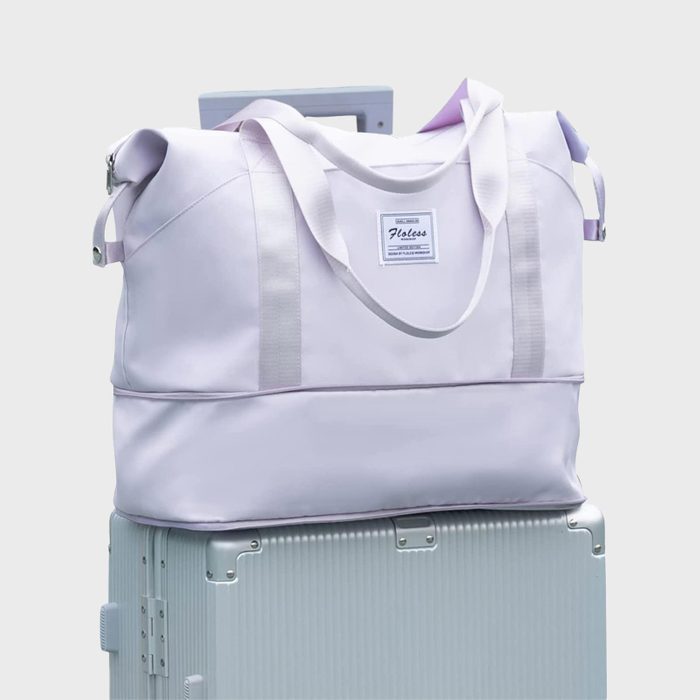 A light purple duffel bag sits on a ribbed suitcase, against a plain background. A patch reads 