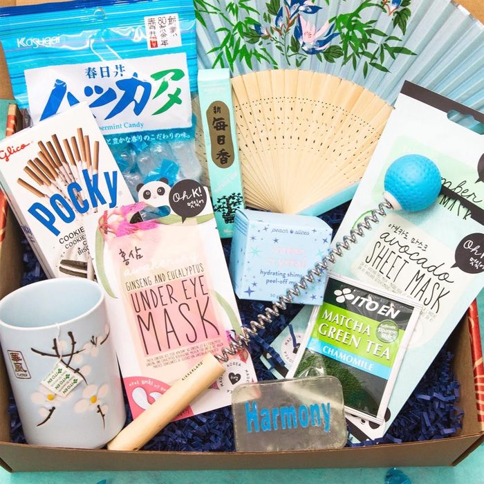 A gift box displays skincare items, snacks, tea, and a decorative fan, arranged on blue paper. Visible text: 