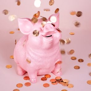 Pink piggy bank surrounded by falling coins, set against a soft pink background.