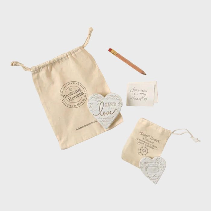 Heart-shaped ceramic pieces rest on drawstring bags, accompanied by a pencil and a note saying, 