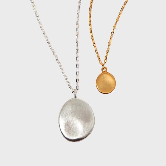 Two disc pendants hang on chains; one is silver, the other gold; suspended against a plain, light background.