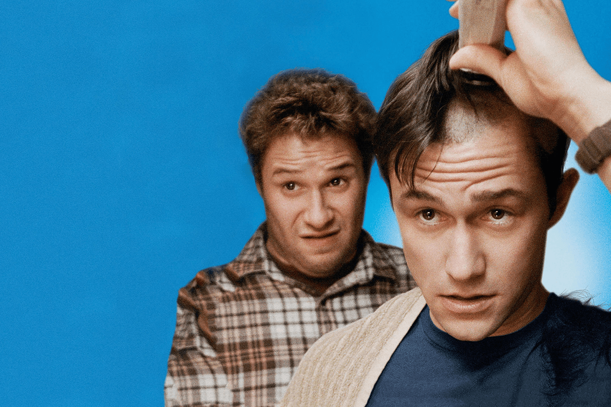 A man shaves his head with clippers while another looks surprised, set against a solid blue background.