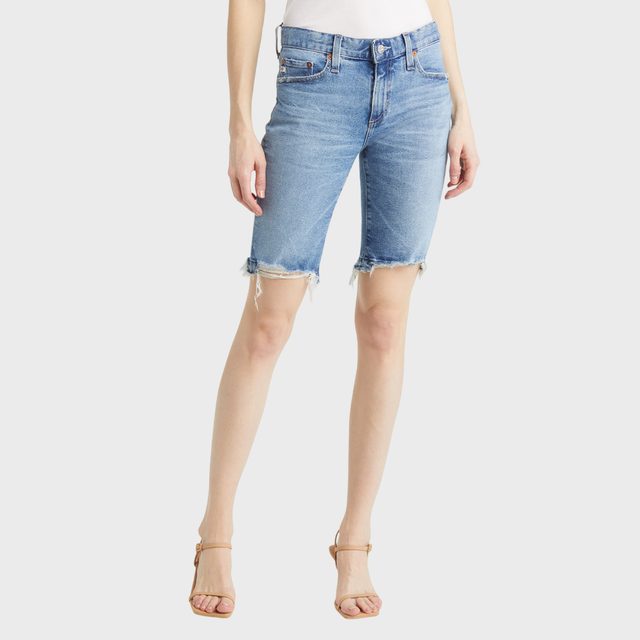 Denim shorts are worn by a person standing in minimalist context, featuring frayed hems and a slightly faded blue color.