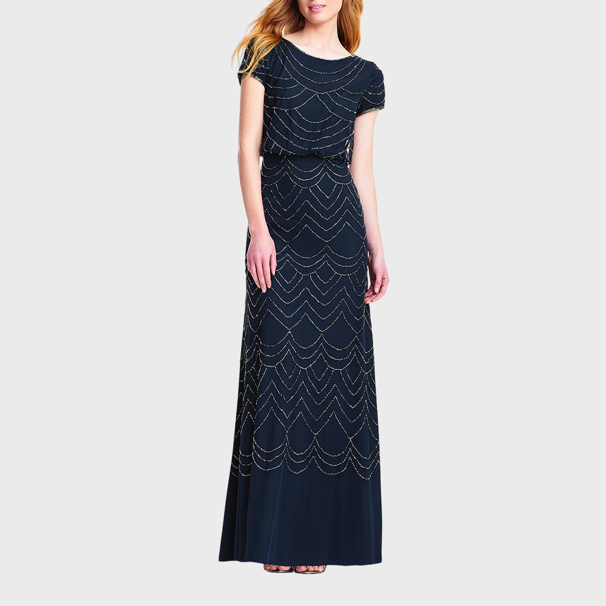 Woman wearing a long navy dress with beaded patterns, standing against a plain gray background.