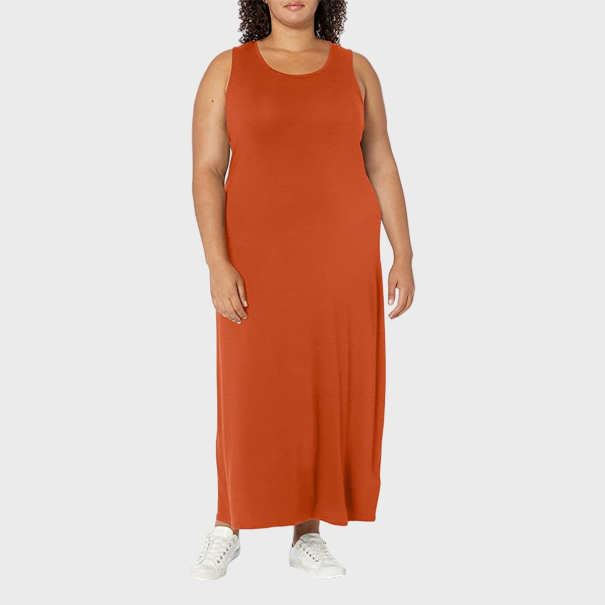 A person stands wearing an orange sleeveless dress and white sneakers, set against a plain light grey background.