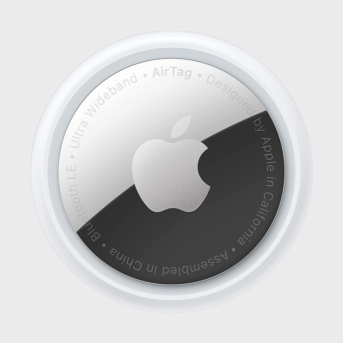 A circular Apple AirTag with a silver logo and engraved text, against a plain gray background.