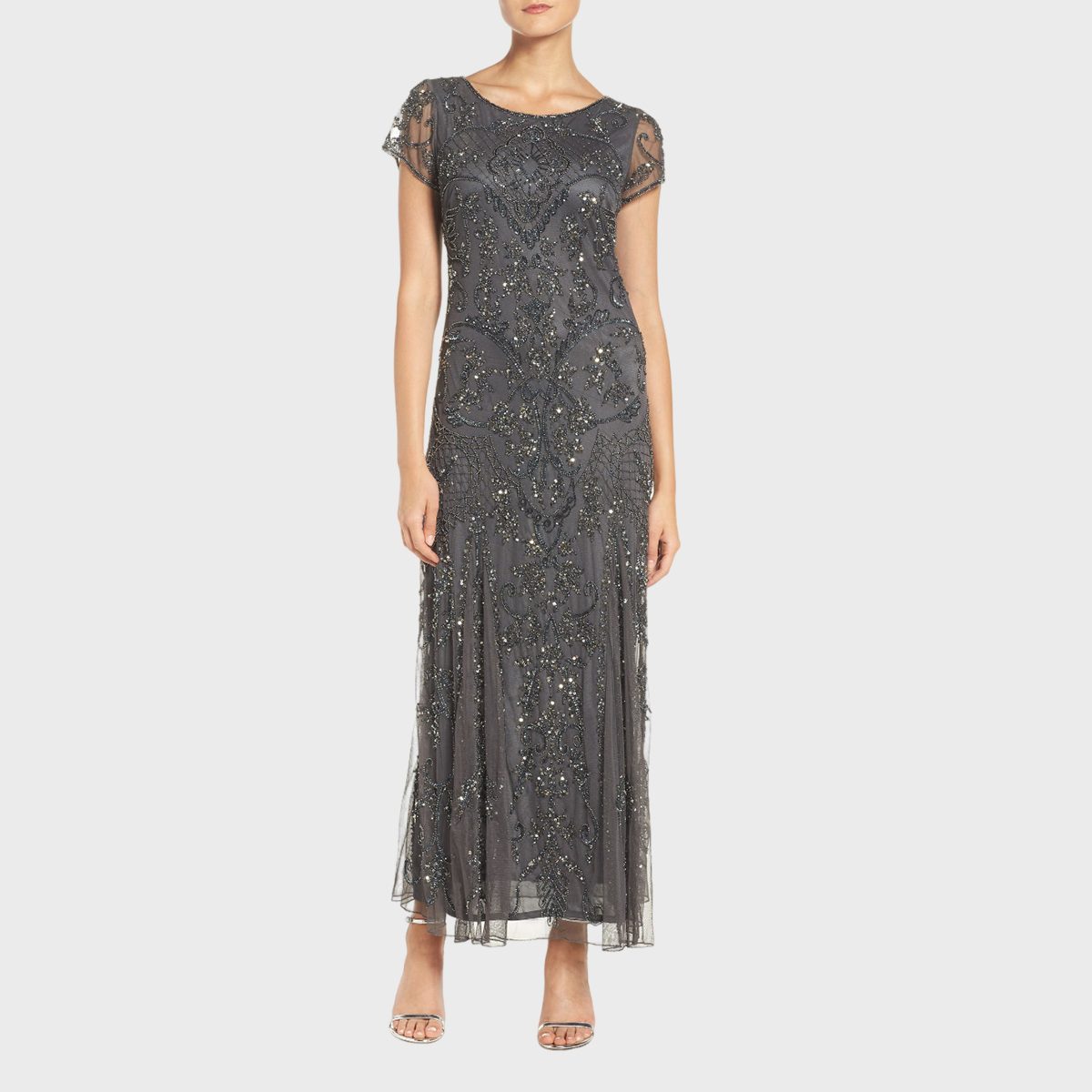 A woman stands wearing a dark, intricately beaded evening gown against a plain white background.
