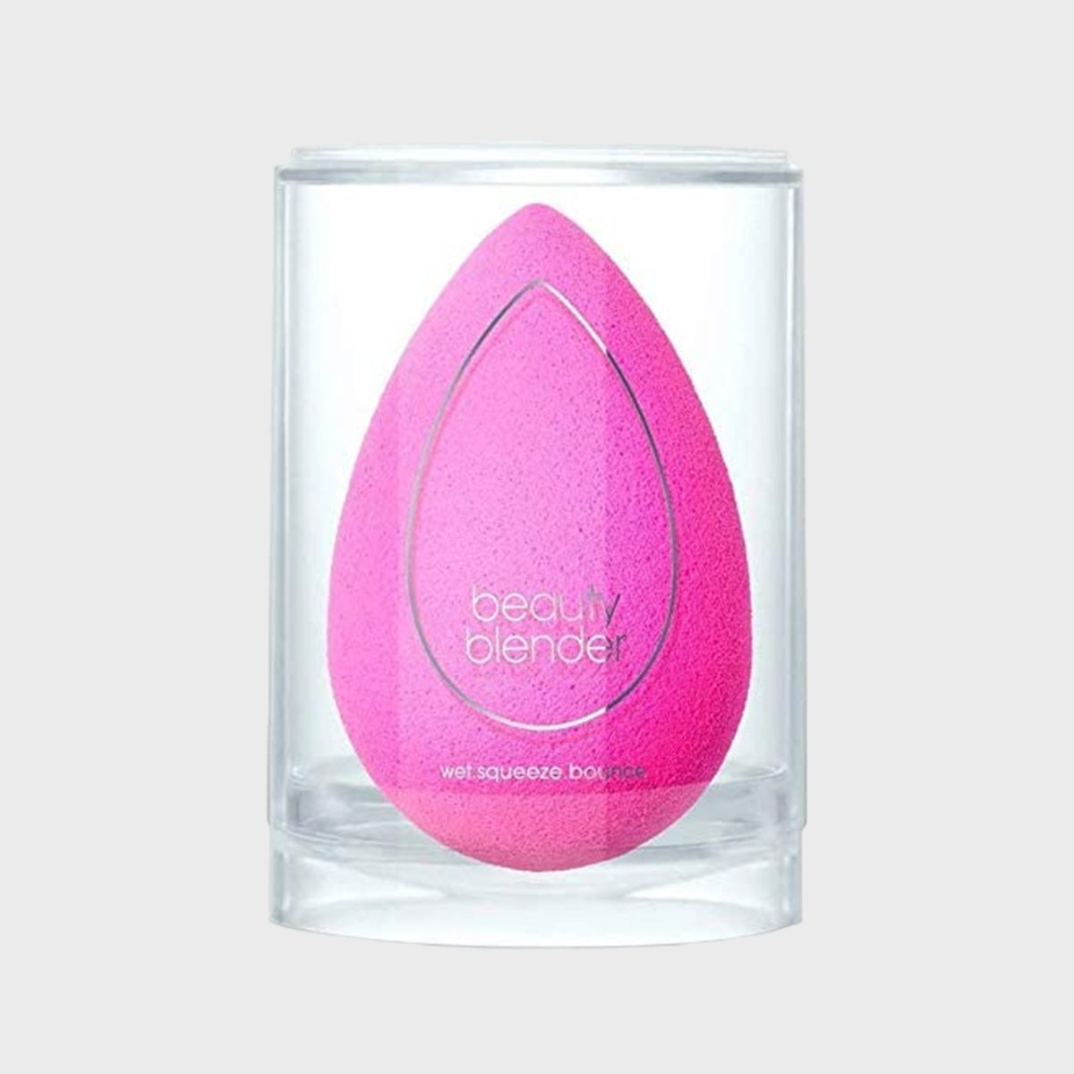 Pink teardrop-shaped sponge rests in a clear cylindrical container, labeled "beauty blender" with instructions "wet.squeeze.bounce." on a light gray background.