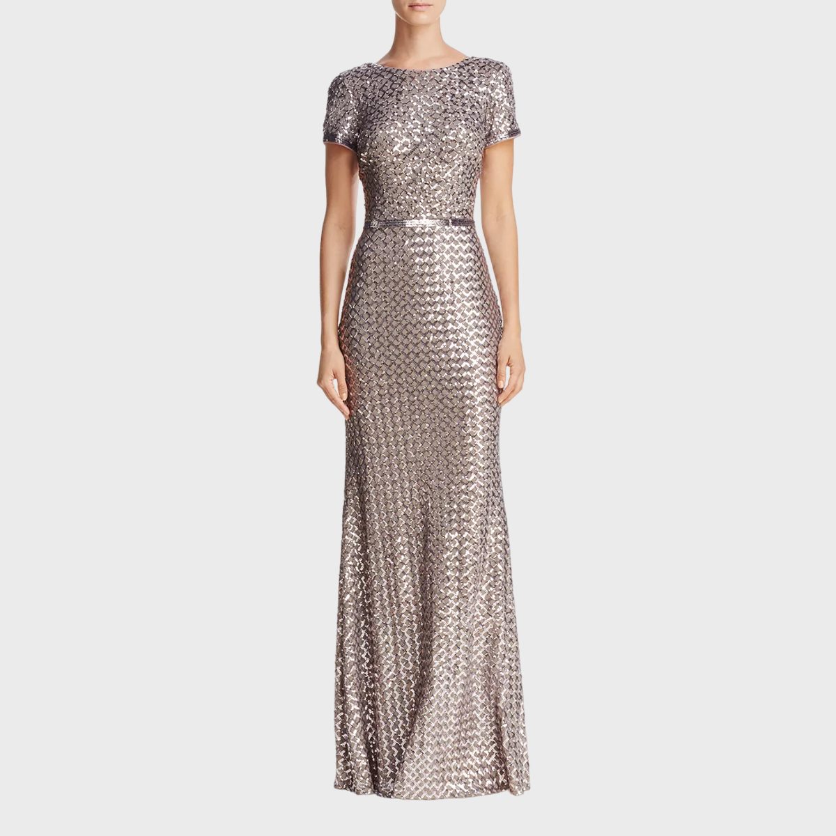 A person wearing a sequined, floor-length silver gown stands against a plain backdrop.