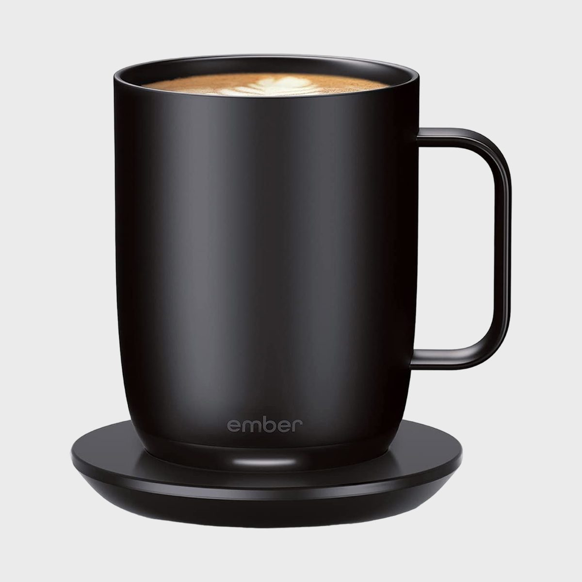A black smart mug rests on a round charging base, featuring latte art. Text: "ember."