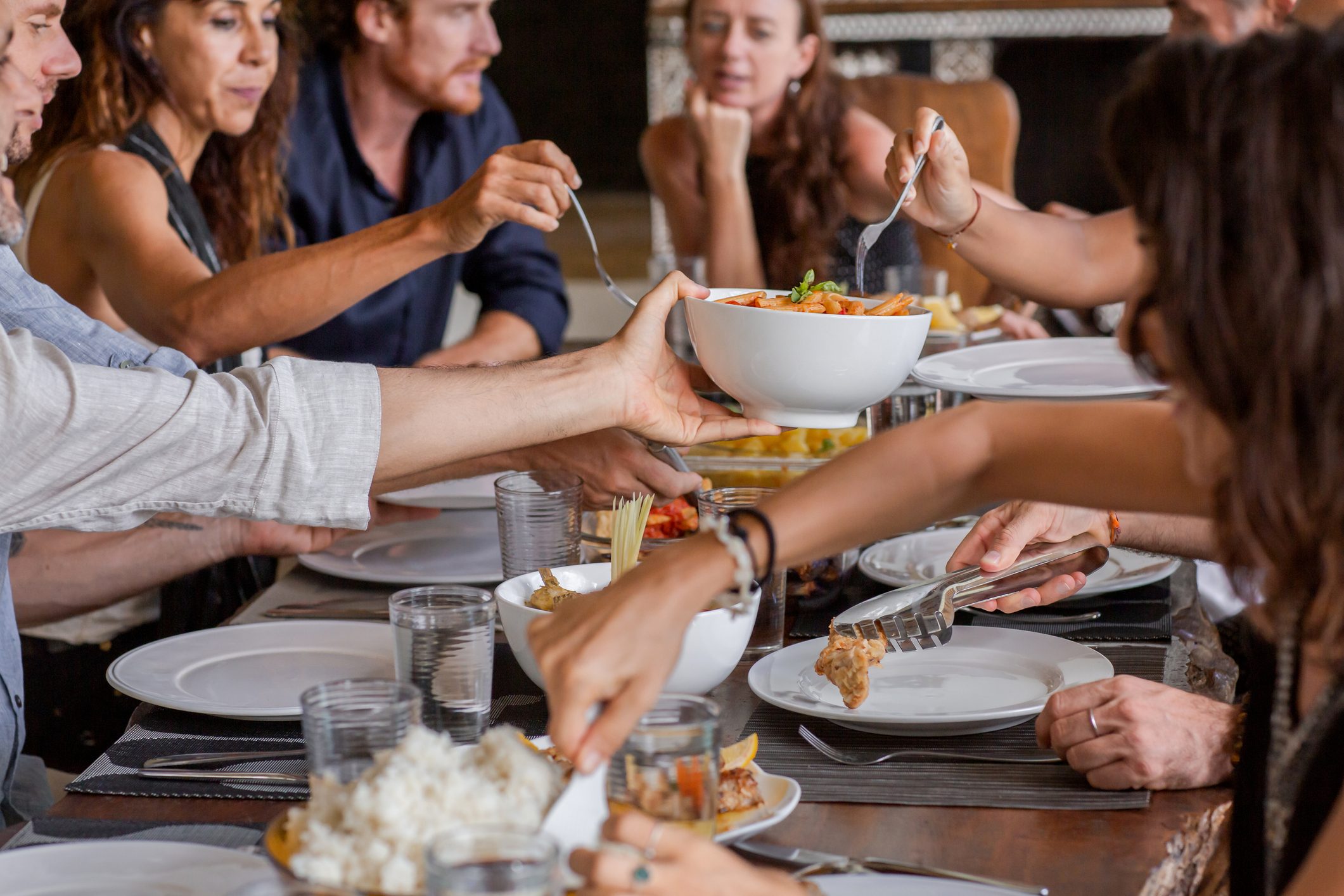 Diverse group of multiethnic friends enjoying meal sharing and passing food to each other in outdoor cafe or home. Leisure, food and drinks, people and holidays concept