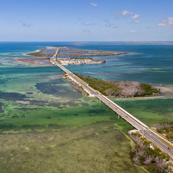 Road stretches across a series of small islands and turquoise waters under a clear blue sky, linking distant landmasses.
