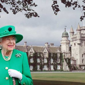 A woman in a green outfit stands smiling, holding a cane, with a large castle and tree branches in the background.