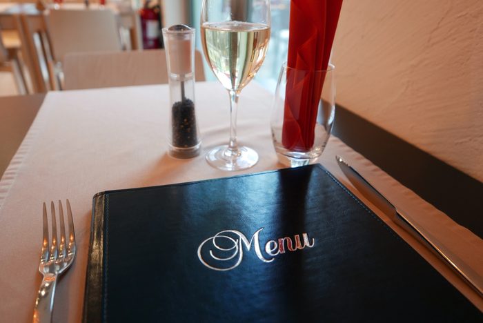 Menu By Pepper Shaker And White Wine On Table In Restaurant