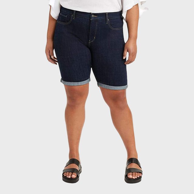 Person wearing dark denim shorts, standing with hands relaxed in a neutral pose against a plain, light background.