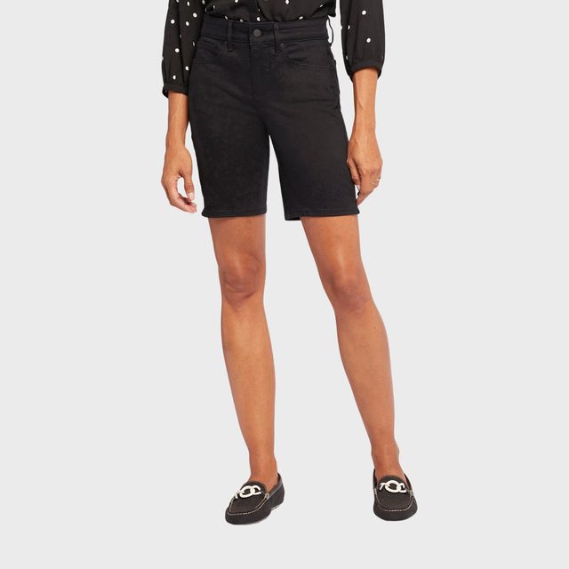 Person stands casually, wearing black shorts, a polka dot blouse, and loafers, against a plain white background.