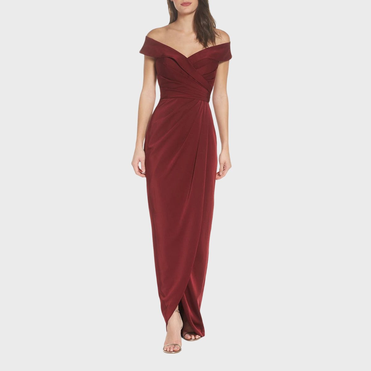 A woman models a burgundy off-the-shoulder gown, standing against a plain white background.