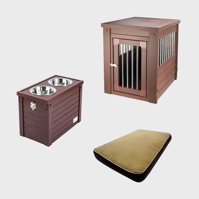 Brown dog crate, holding a bed, surrounded by a two-bowl stand with stainless steel dishes, on a light background.