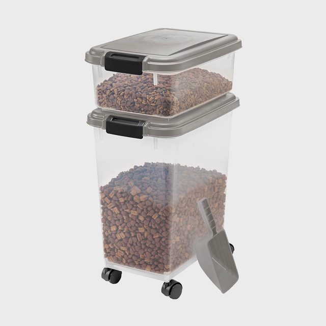 Transparent containers hold pet food, stacked on top of each other with grey lids, alongside a scoop; situated on a plain background.