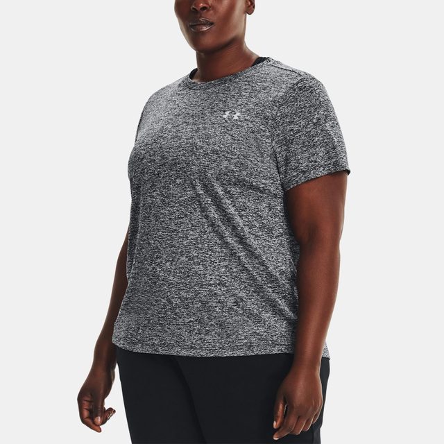Person wearing a gray speckled T-shirt stands slightly turned; under calm lighting, showcasing the logo on the chest, against a plain background.
