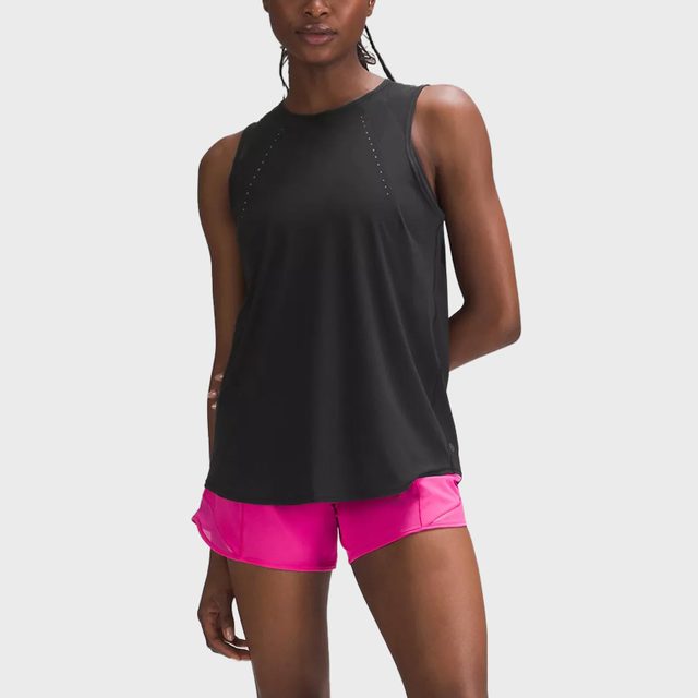 Person standing; wearing a black sleeveless top and bright pink shorts; posing against a plain white background.