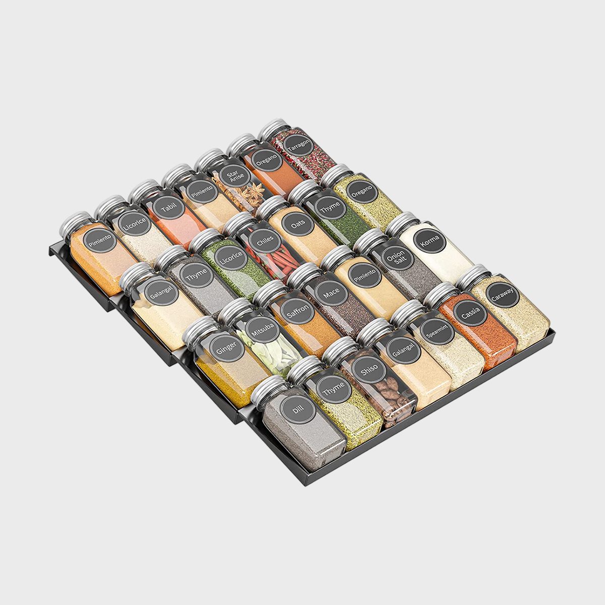 Glass jars sit organized, labeled with various spices, displayed on a tiered black rack against a plain background.