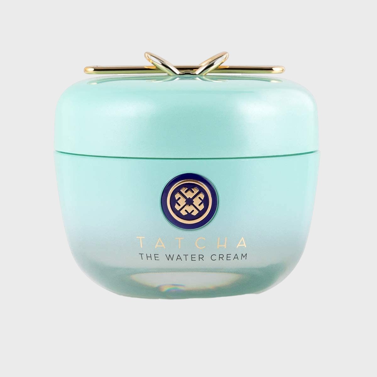 Aqua-blue jar sits, displaying "Tatcha The Water Cream" text, adorned with a gold decorative lid, against a plain gray background.