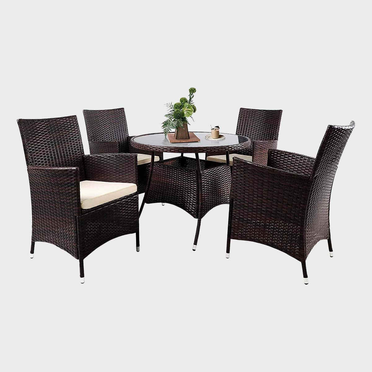 Wicker dining set with four chairs surrounds a glass-top table, featuring a decorative plant centerpiece in an indoor or outdoor setting.