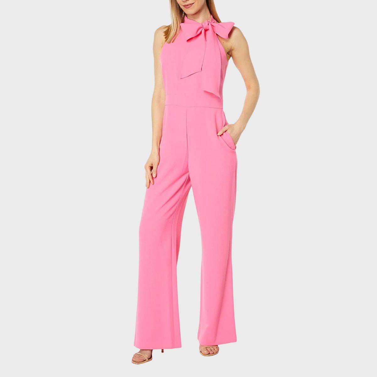 A person wears a pink jumpsuit with a bow, standing gracefully against a plain white background.