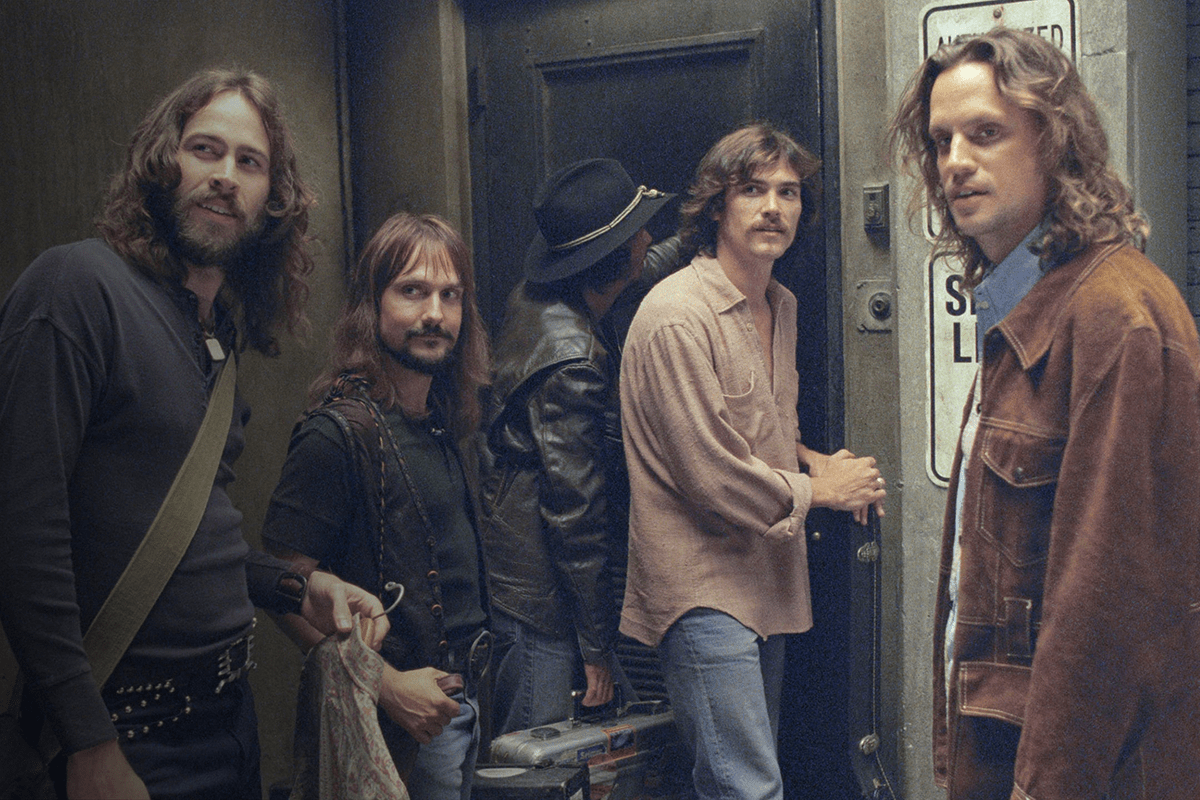 Five men stand outside a door, one holding a bag near a "Standard Level" sign, in a dimly lit hallway.