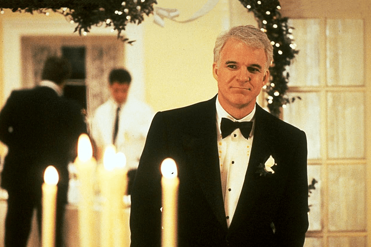 A man in a tuxedo stands smiling; elegant candles and a festive indoor background create a formal event setting.