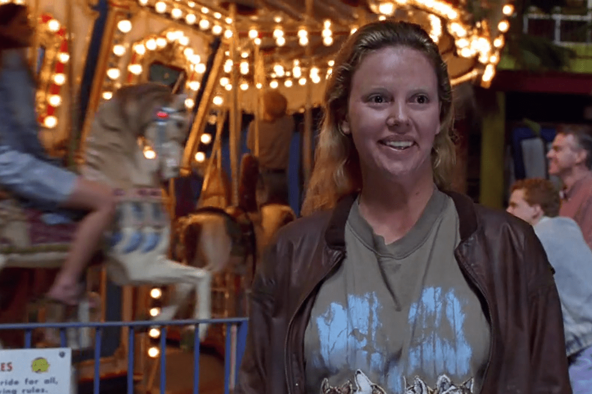 Person smiling near a carousel with brightly lit horses in a lively amusement park environment.