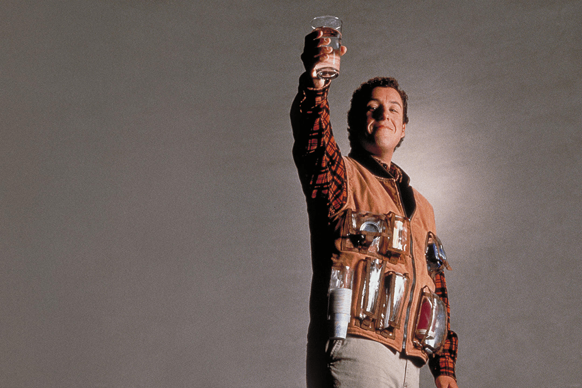 A person raises a drink with a confident expression, wearing a vest filled with multiple beverage containers, set against a plain background.