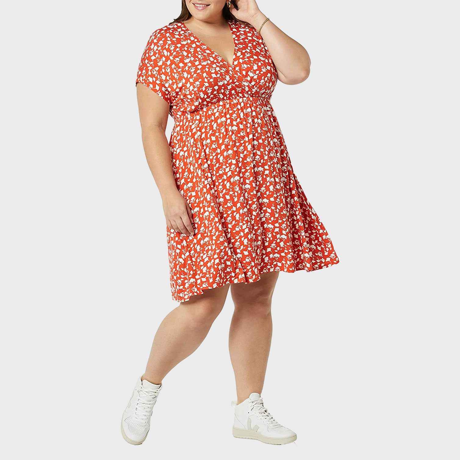A person wears an orange floral dress and white sneakers, posing confidently against a plain background.
