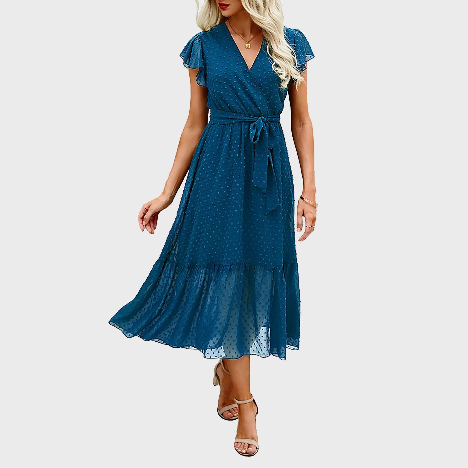 Woman wearing a blue, polka-dot, short-sleeve, wrap dress with a waist tie, standing against a plain gray background.