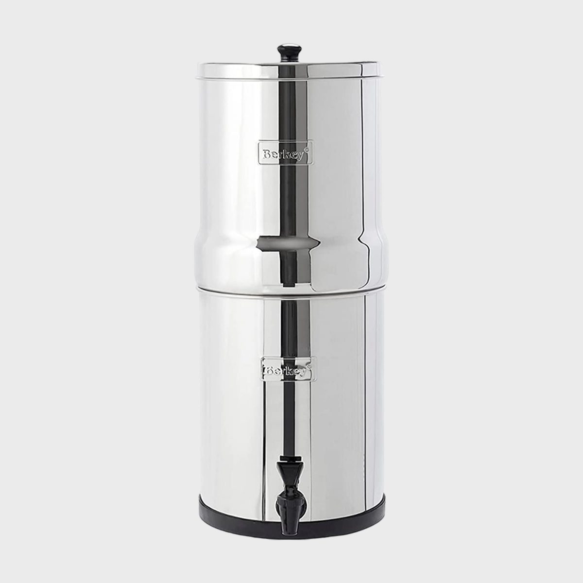 Stainless steel water filter sits upright with a spigot, set against a plain gray background. "Berkey" is written on the two containers.