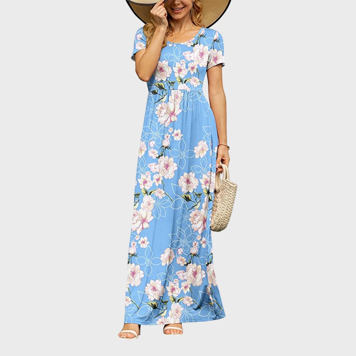 Woman wearing a blue floral maxi dress holds a straw handbag, with a large sun hat partially covering her face against a plain background.