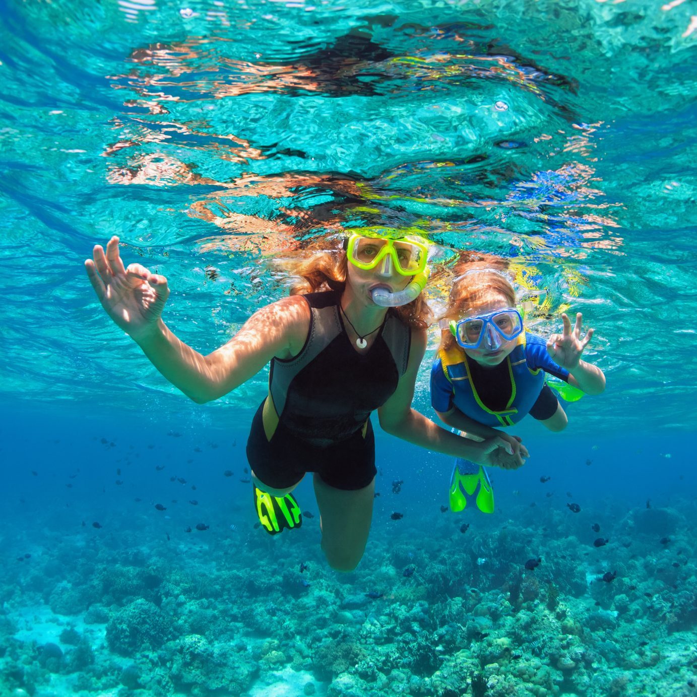 Mother, kid in snorkeling mask dive underwater with tropical fishes