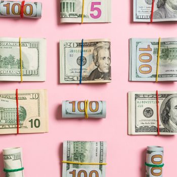 Bundles of U.S. currency wrapped with rubber bands are arranged on a pink background.