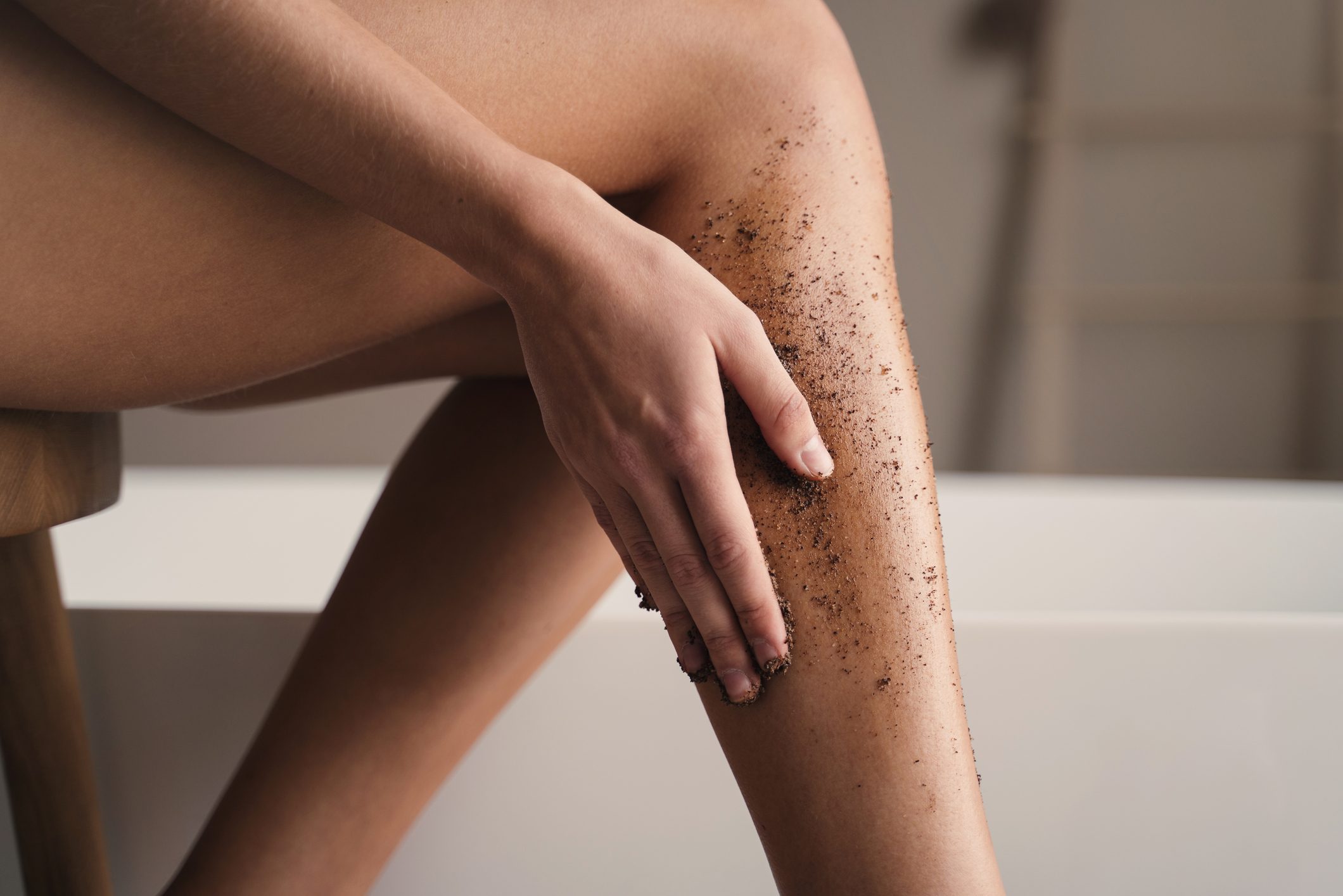 Close-up of woman hand scrubbing legs in bathroom during anti-cellulite massage with coffee scrub
