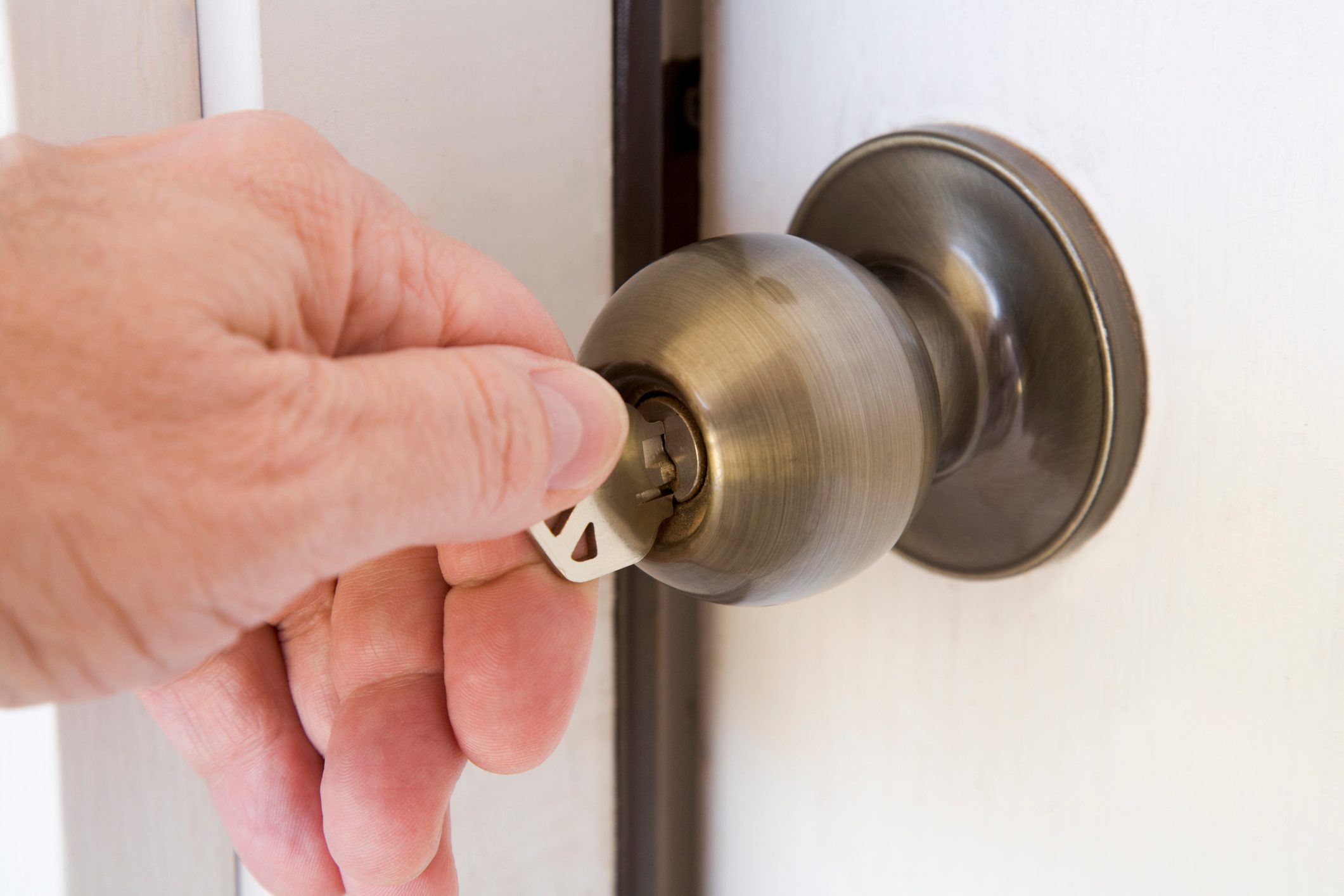 A hand turning a key in a brass doorknob, set in a white door, capturing the action of unlocking.
