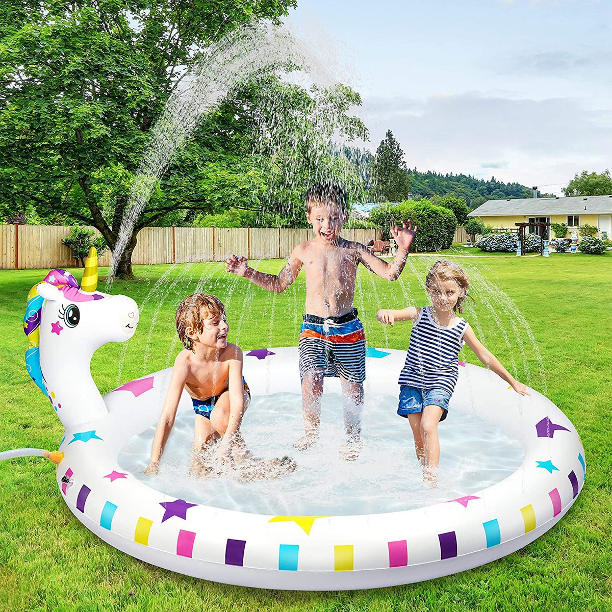 Children play joyfully in a unicorn-shaped inflatable pool, spraying water in a sunny backyard surrounded by trees and houses in the background.