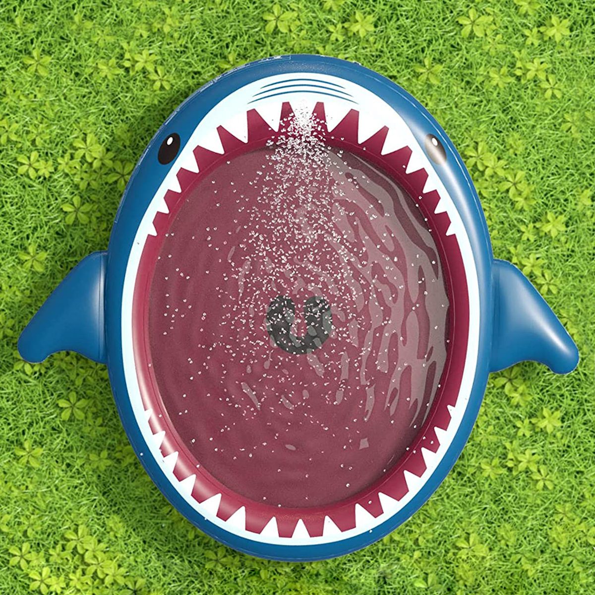 A circular shark-shaped splash pad sprays water, set on a grassy surface.