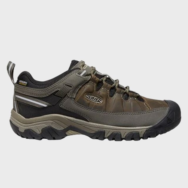 A rugged hiking shoe sits side view, featuring brown leather, grey accents, and robust black sole, suited for outdoor adventures.