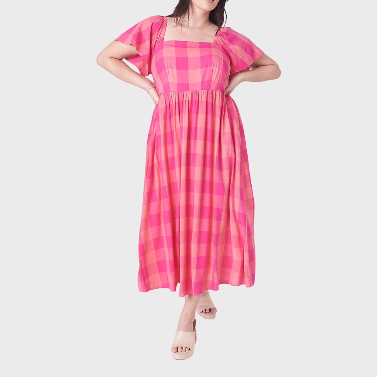 A person wearing a pink checkered dress stands with hands on hips against a plain white background.