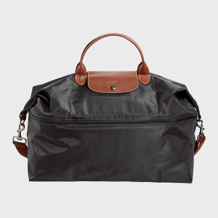 A black duffel bag sits with brown leather handles and a flap, against a plain white background.