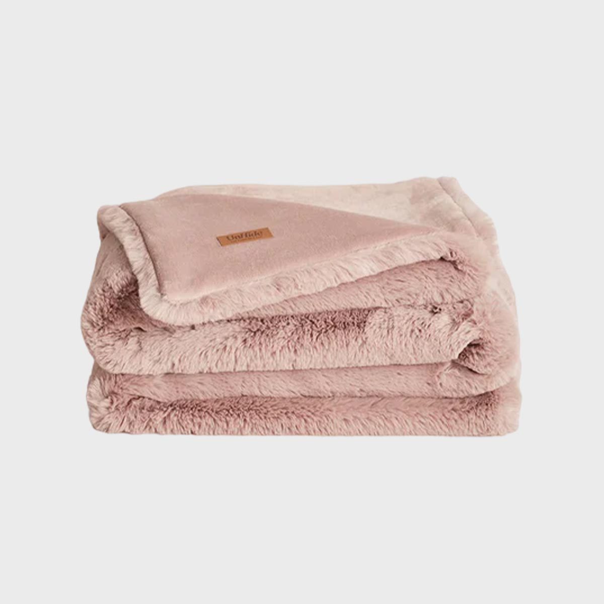 A folded, fluffy pink blanket rests neatly against a plain white background. A small, leather tag reads "Barefoot Dreams."