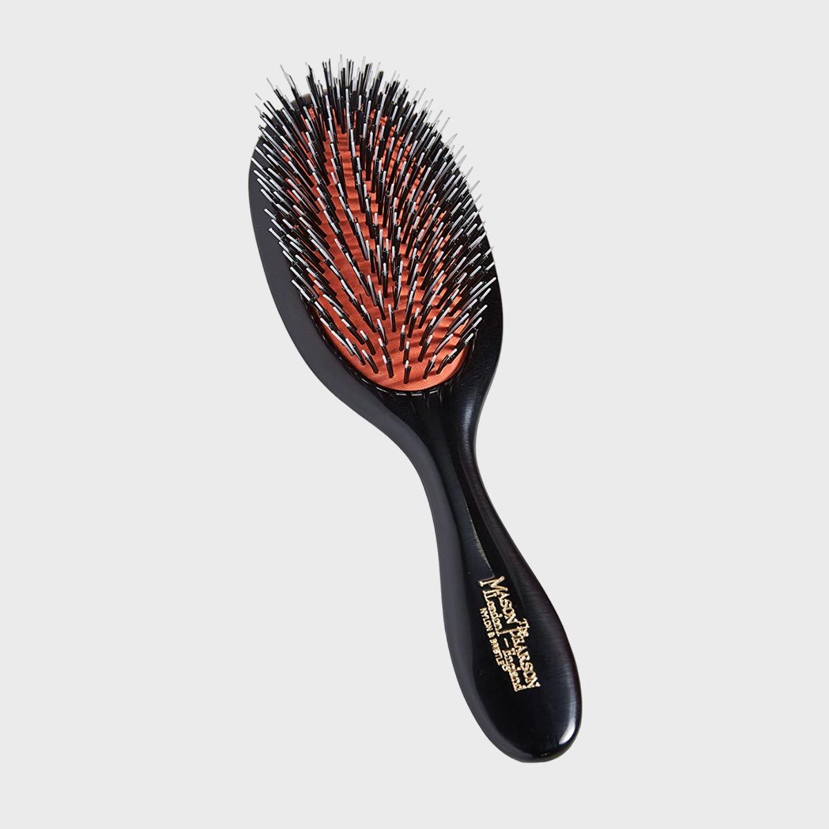 A black hairbrush with fine bristles on a red cushion, labeled "Mason Pearson," rests against a plain white background.